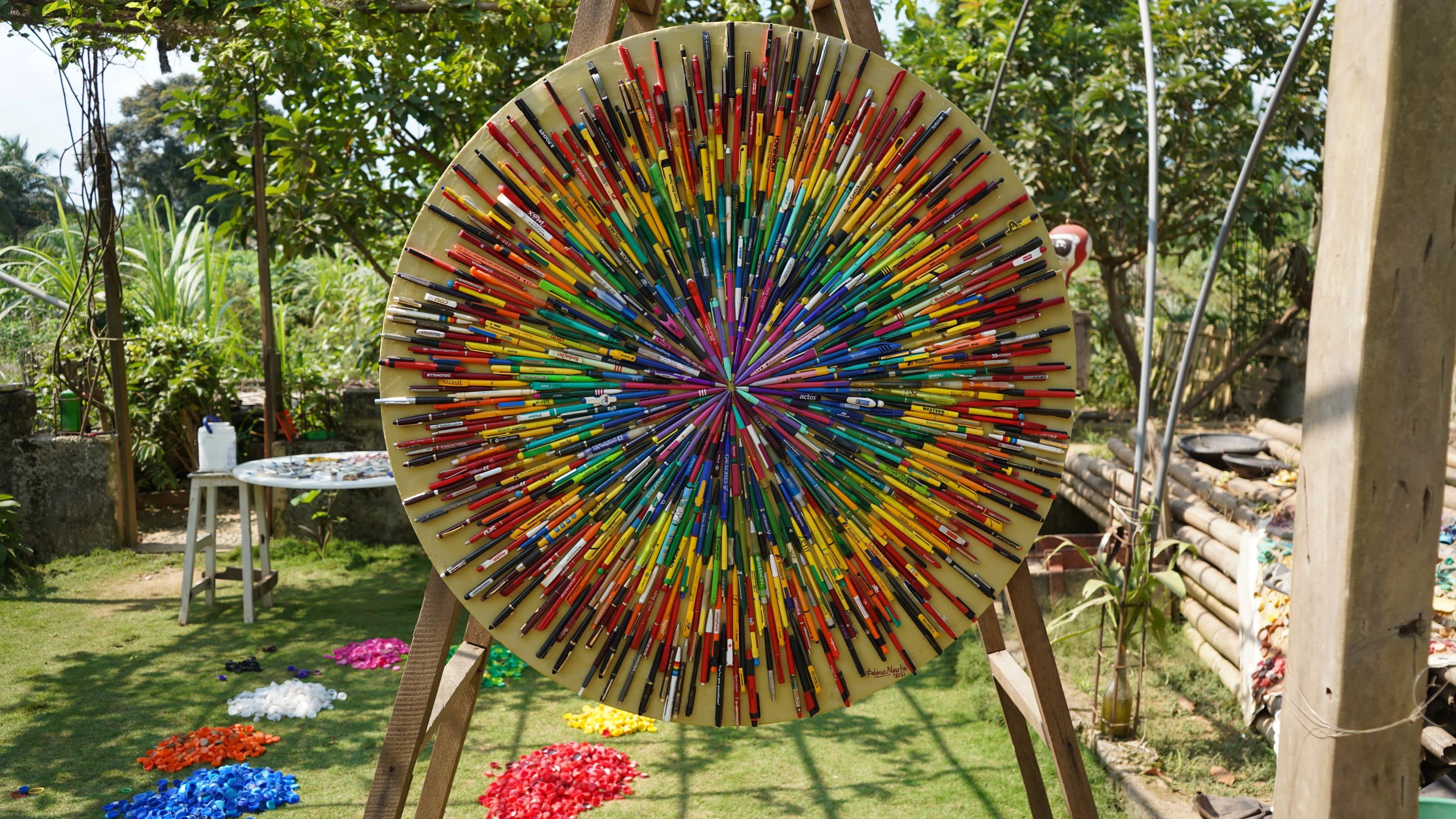 Kobina Nyarko's disc of ballpoint pens glued in a starburst, on an easel in the studio garden